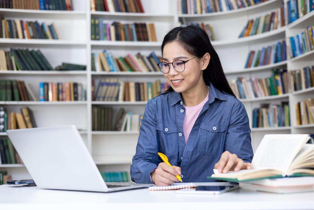 Profissional focada trabalhando com notebook em uma biblioteca ou escritório organizado.