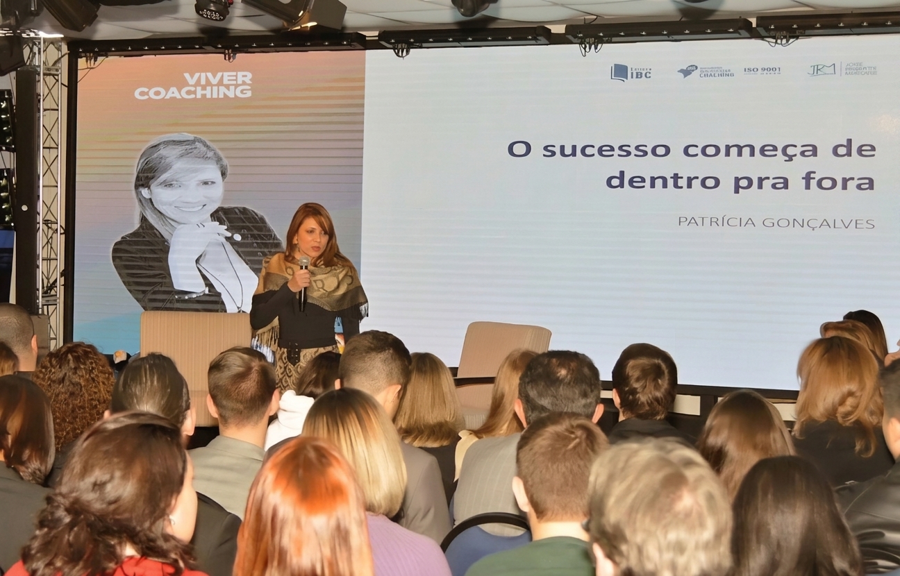 Patrícia Gonçalves em palco com tela exibindo o sucesso começa de dentro pra fora